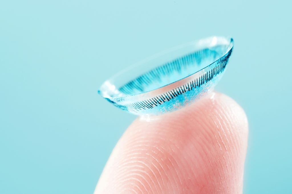A person's finger with a small soft contact lens on it.