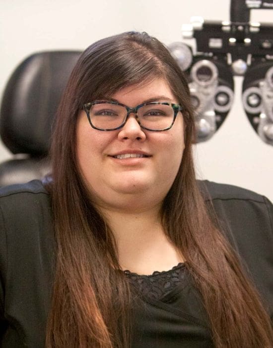 A woman with glasses smiling in front of an eye exam machine in Boise.