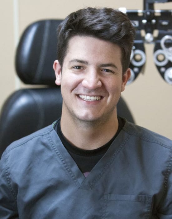 A smiling healthcare staff member in scrubs with ophthalmology equipment in the background at Idaho Falls.