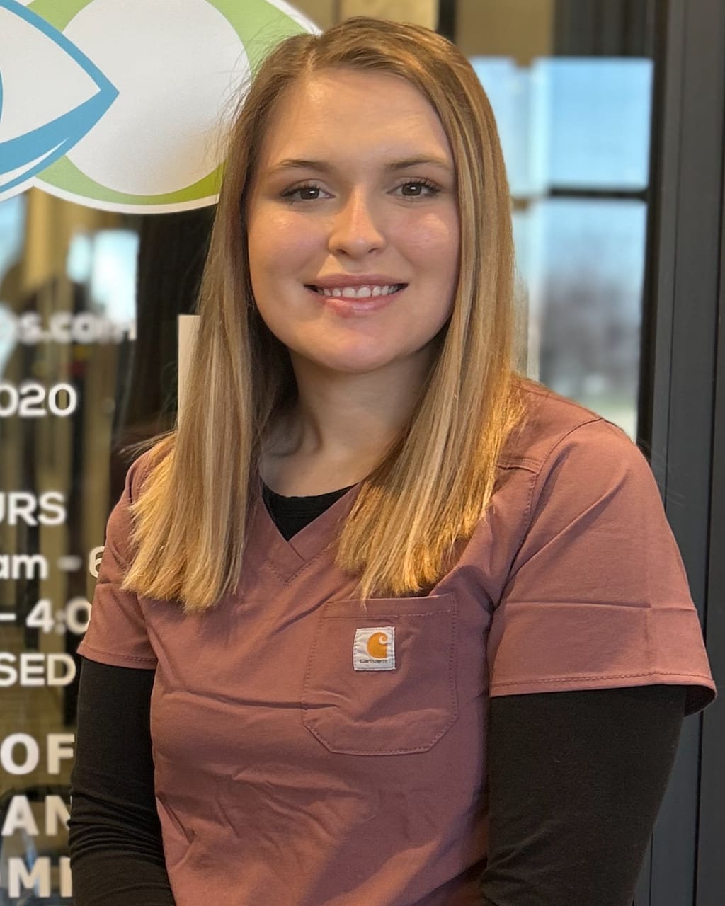 A woman in scrubs standing in front of an Optometrist Nampa sign.