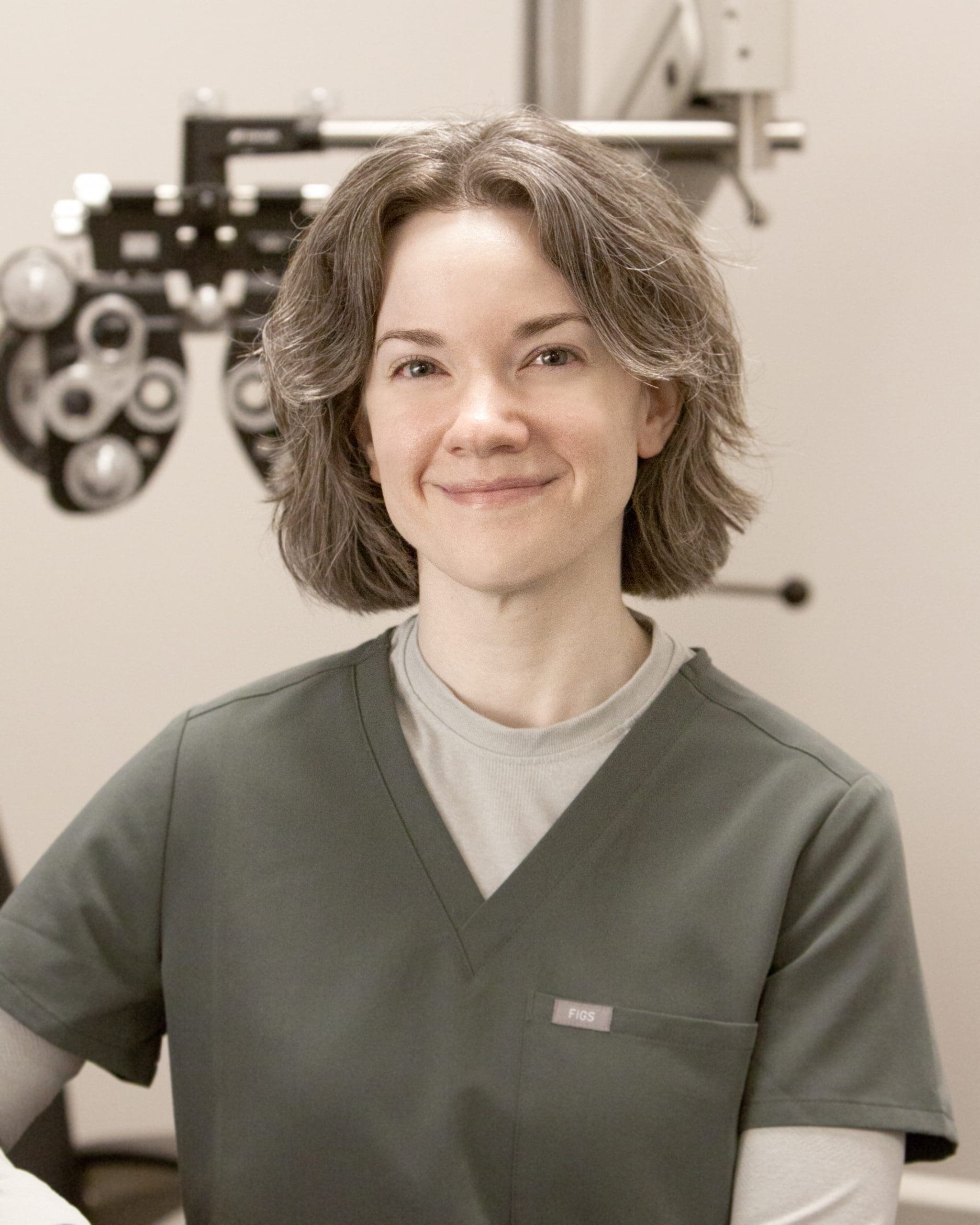 An optometrist in Pocatello, smiling in front of a microscope, is wearing scrubs.