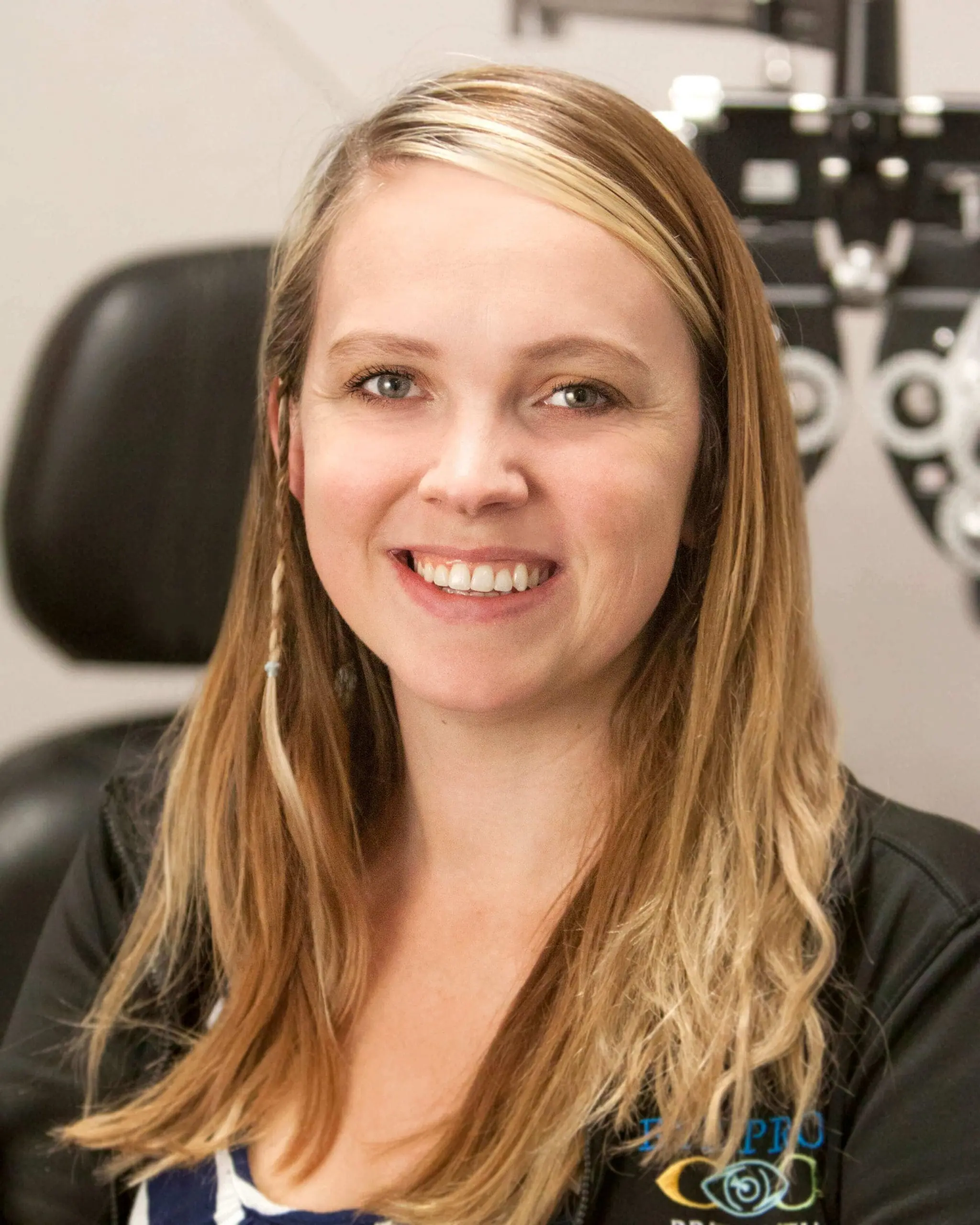 A woman smiling in front of an eye exam machine, benefiting from professional administrative services.