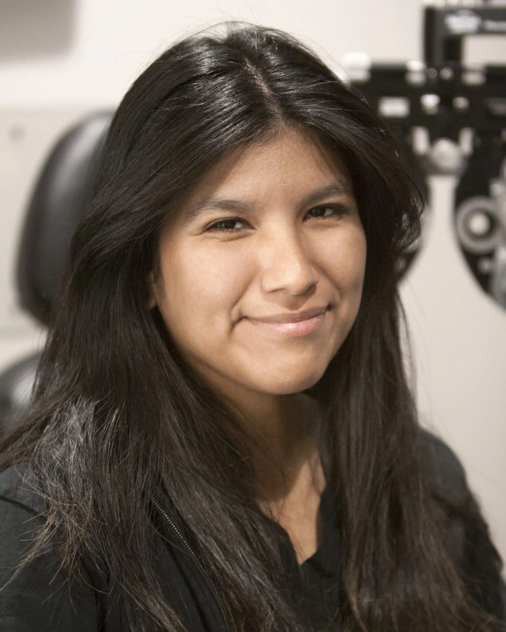 A young woman smiling in front of an eye exam at Optometrist Layton.