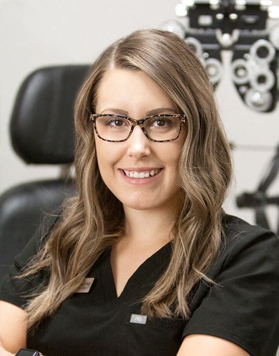 A staff member in glasses is standing in front of an eye exam machine in Nampa.