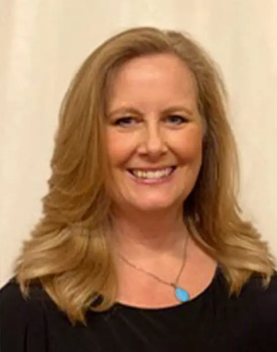 A smiling woman from the management team with long blonde hair and a black top against a light background.