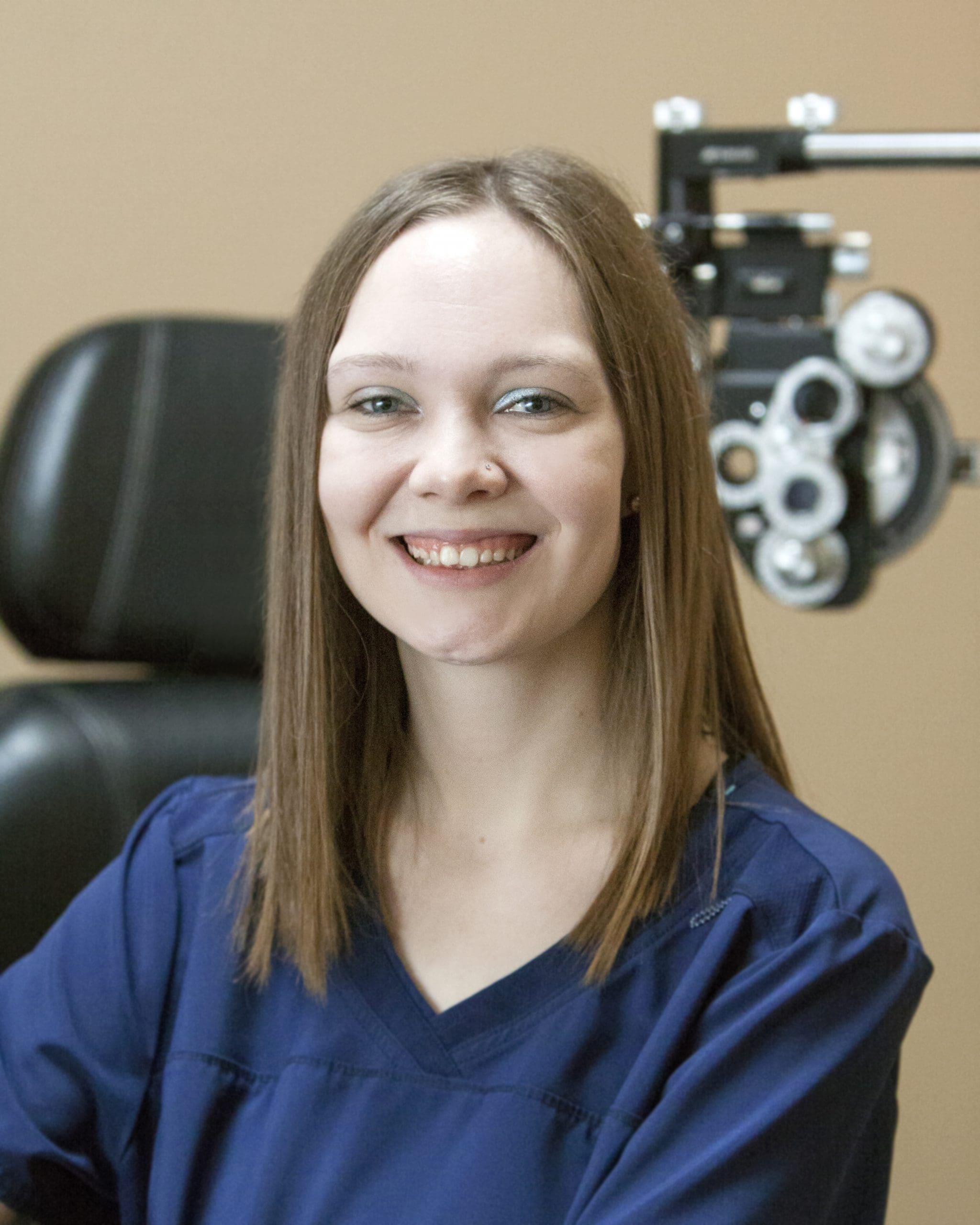 A woman smiling in front of an eye exam machine at an optometrist's office in Idaho Falls.