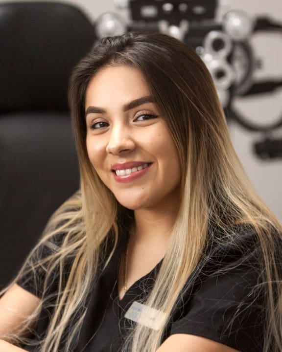 A young woman smiling in front of a pair of eyeglasses at the Optometrist Logan office.