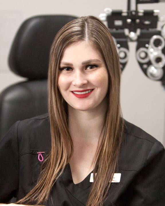 A woman in a black shirt is smiling in front of an optometrist in Logan.