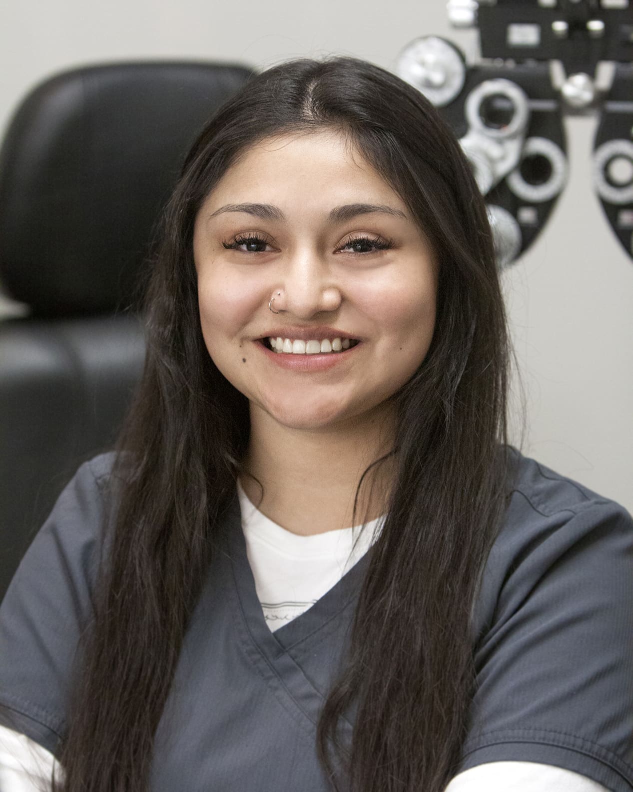 A smiling woman sitting in front of an eye chart at an Optometrist in Twin Falls.