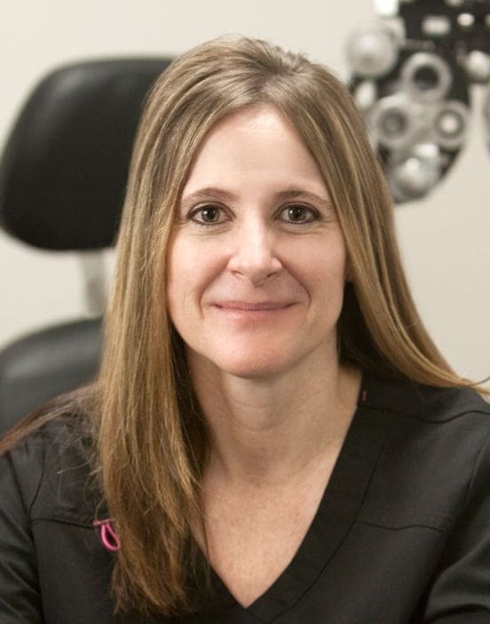 A smiling woman with long hair sitting in front of an optometrist's eye chart at the Ogden-staff clinic.