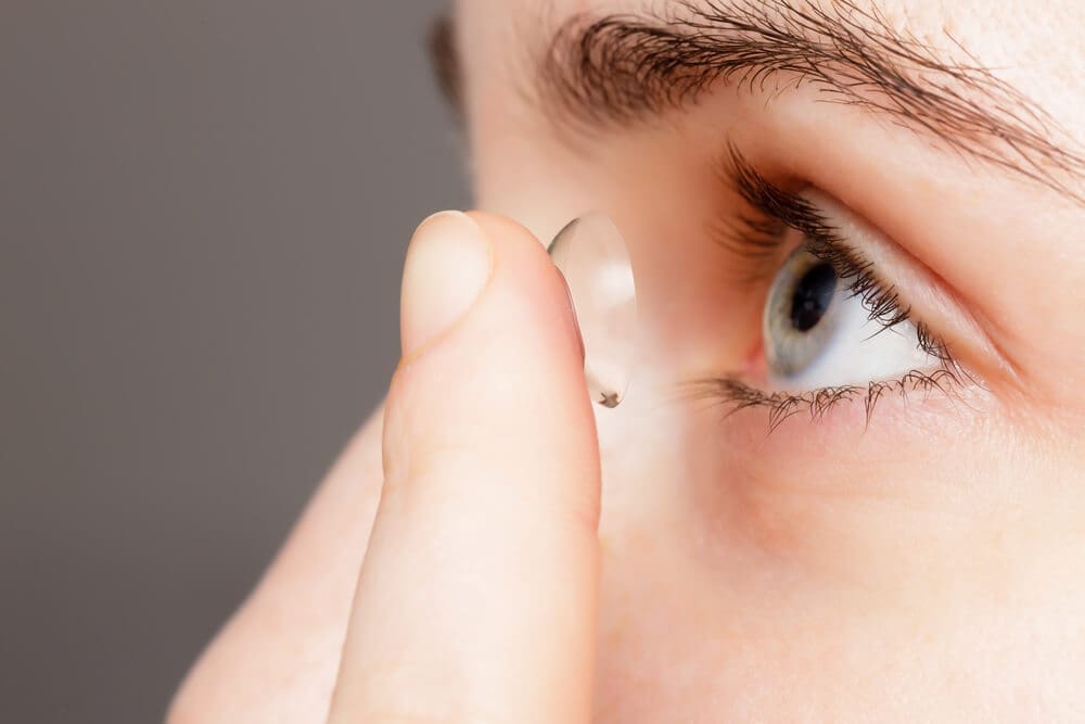 Person inserting a contact lens into their eye for vision correction.