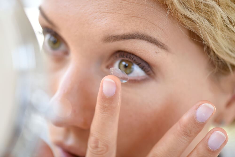 Woman inserting a contact lens into her eye for vision correction.