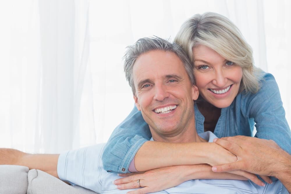 Smiling middle-aged couple embracing in a bright room after their Lasik vision correction.