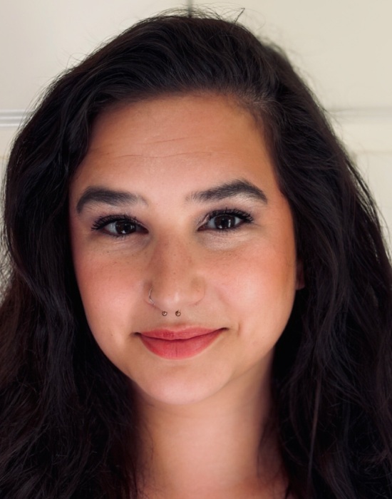 A woman with long, dark hair and a nose piercing smiling slightly, wearing subtle makeup, and facing forward—an image that embodies the warmth and approachability of Patient Services.