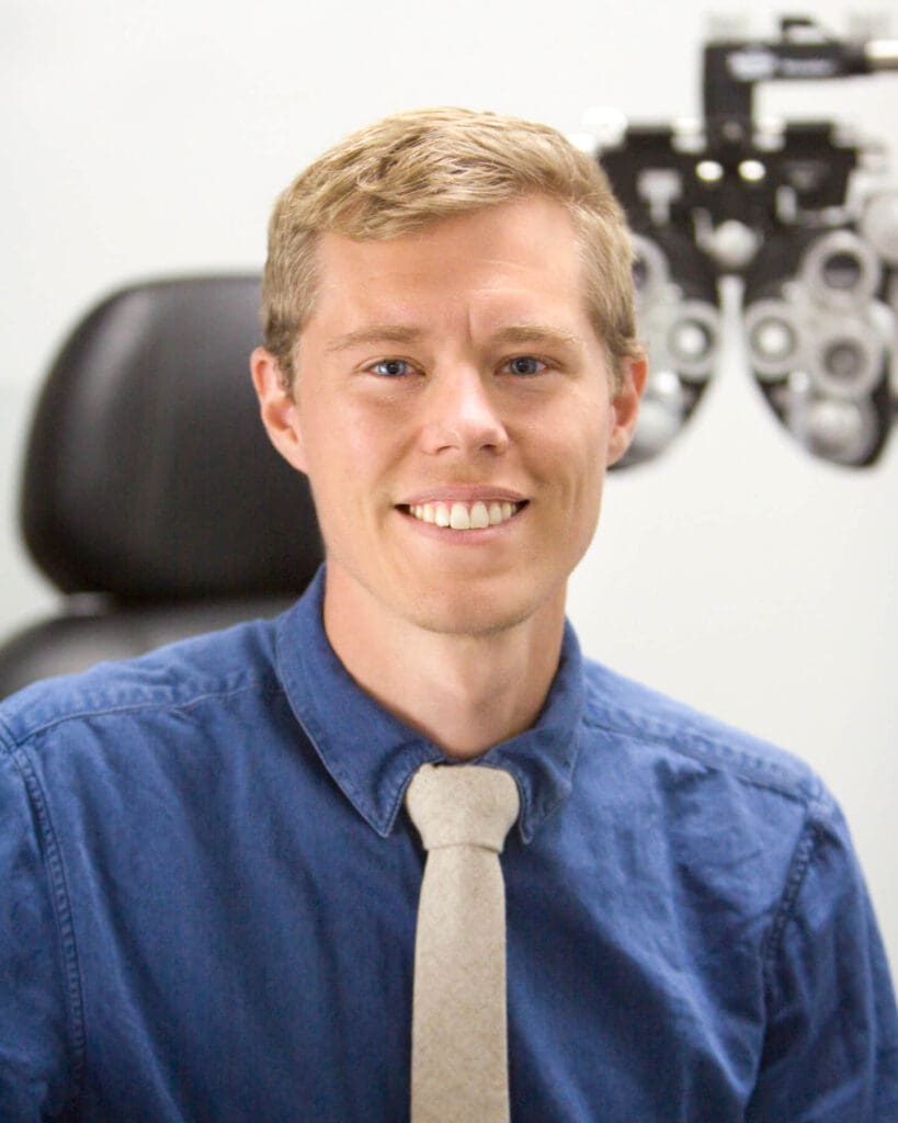 A smiling man with a blue shirt and tie in an optometrist's office, ready to meet our doctors.