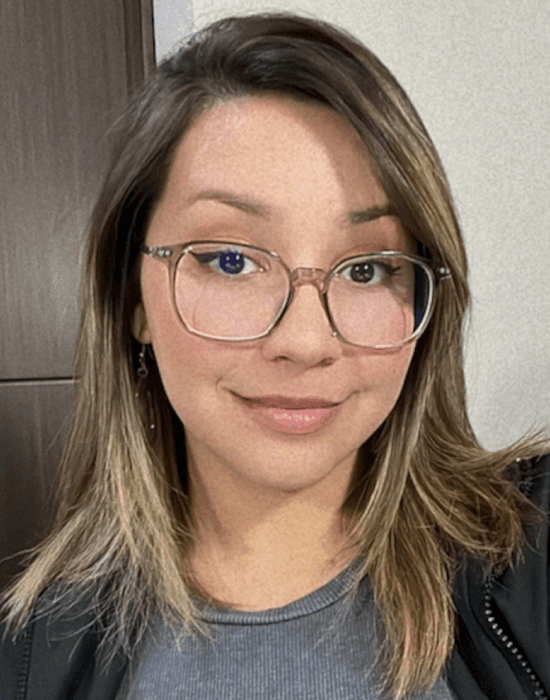 A woman with glasses smiling at the camera in a healthcare setting.