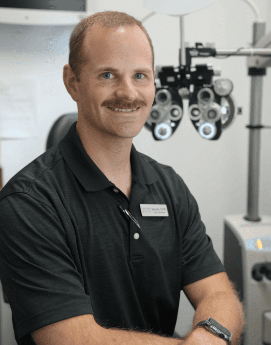 A smiling male optometrist from Eye Pros in a clinic with an eye examination machine in the background.