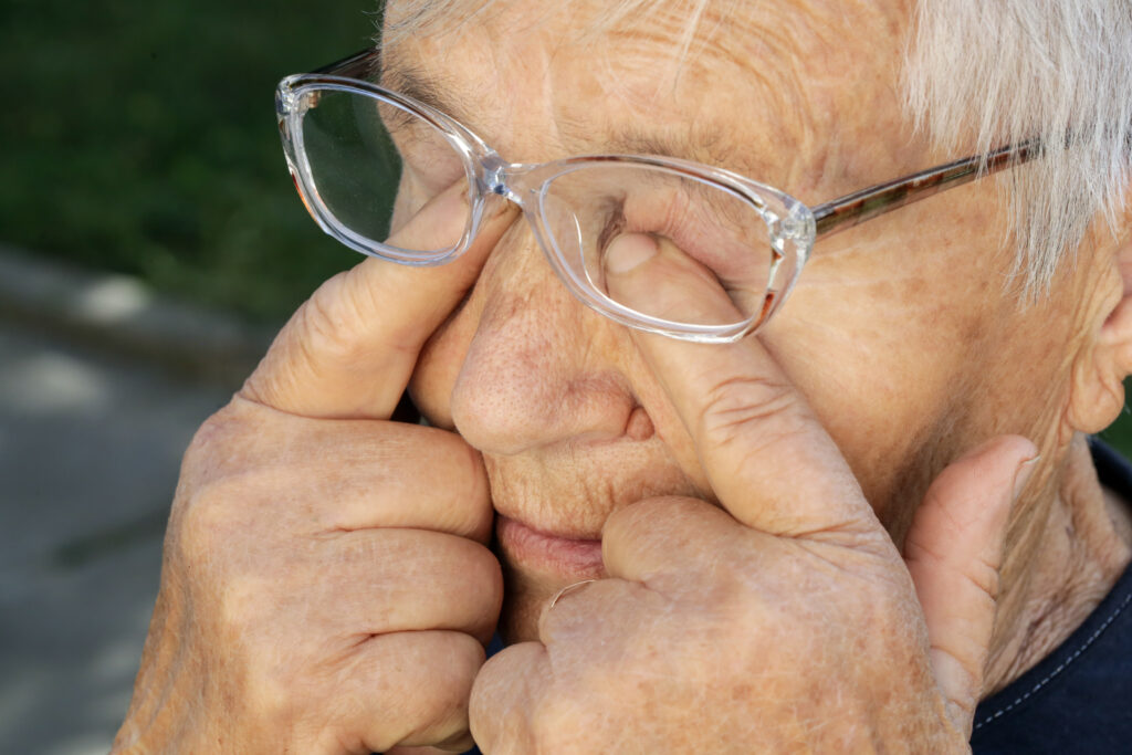 An elderly person wearing glasses rubs their eyes with their fingers outdoors, possibly seeking relief from itchy eyes. For those experiencing similar discomfort, The Eye Pros offer expert advice on relieving itchy eyes effectively.