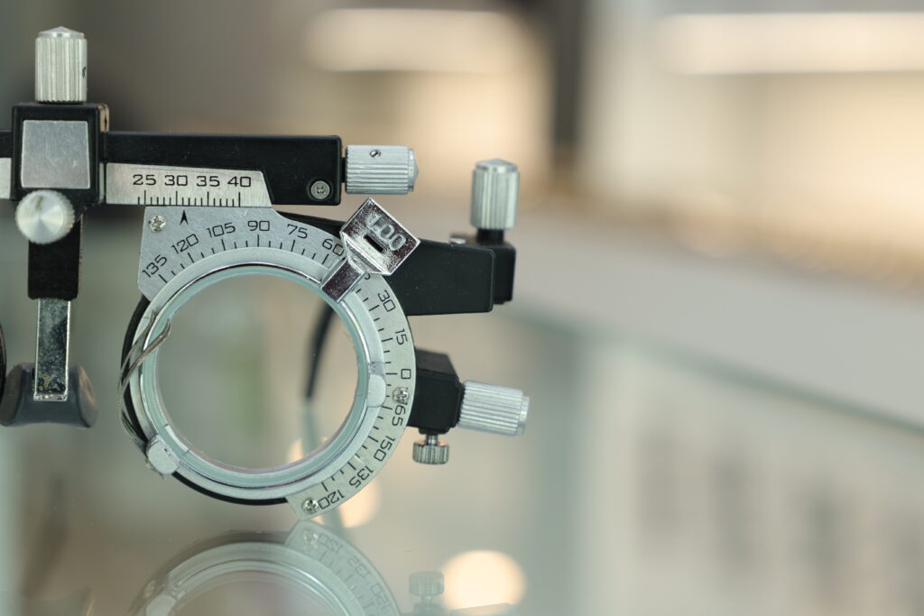 Close-up of a metal optical trial frame with adjustable dials, set on a reflective surface.