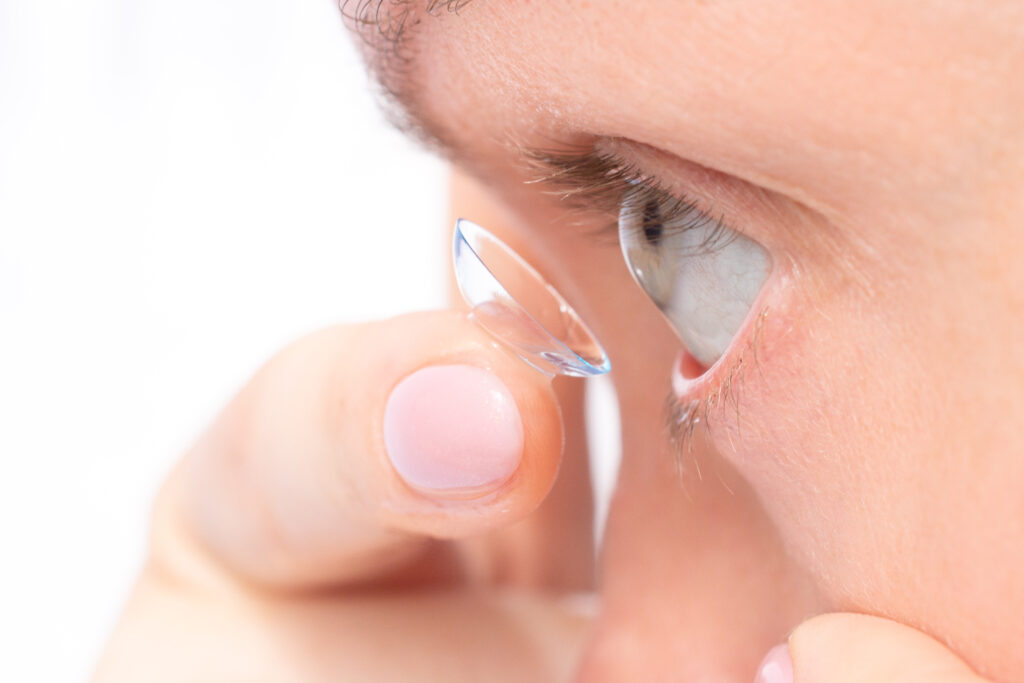 Close-up of a person inserting a contact lens into their eye using fingertips, showing careful placement.