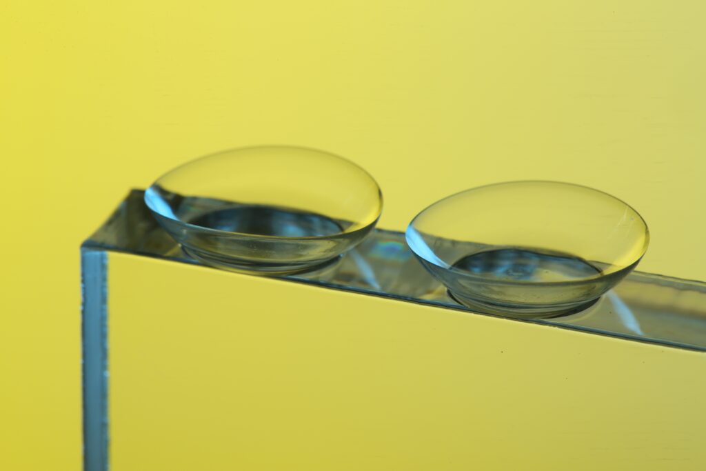 Two contact lenses, like tiny mirrors, rest on a reflective surface against a vibrant yellow background. It's crucial to consider the realities of wearing expired contacts to avoid potential risks to your eye health.