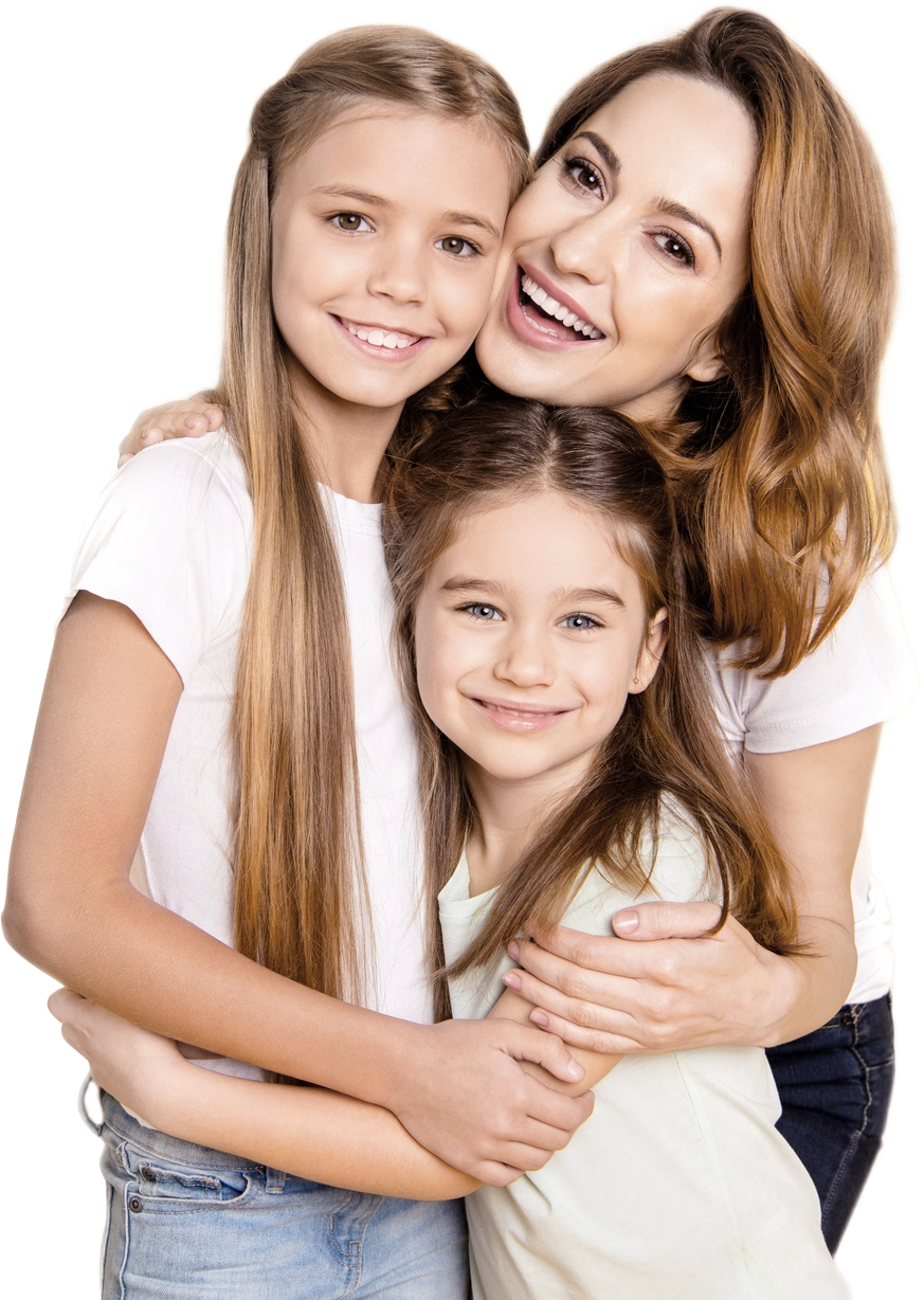 A woman hugs two smiling young girls, all wearing casual light-colored shirts and standing closely together in Idaho Falls, looking at the camera.