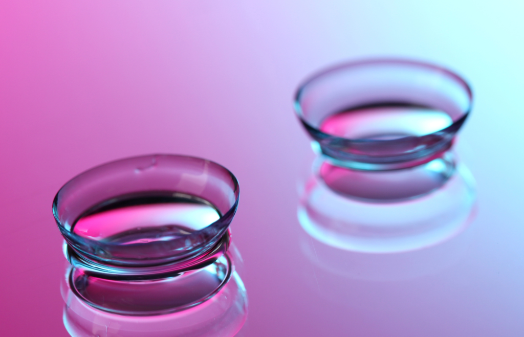Two clear contact lenses are placed on a reflective surface with a pink and blue gradient background, showcasing both comfort and style for those seeking quality contacts in Coeur d’Alene.