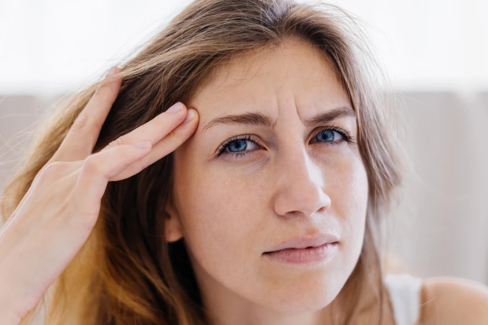 Woman touching her temple with a concerned expression, illustrating discomfort associated with eye strain or dry eyes.