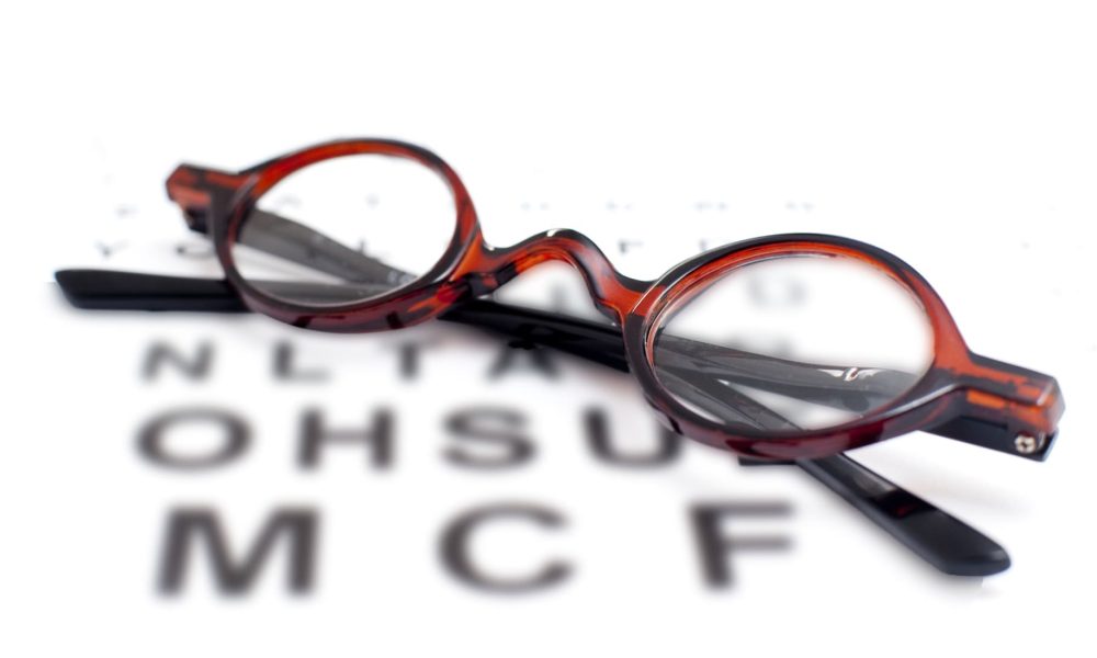 A pair of glasses sits on top of an eye chart, one of the signs you need glasses for vision problems.