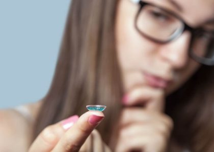 A woman holding a small blue colored contact lens.