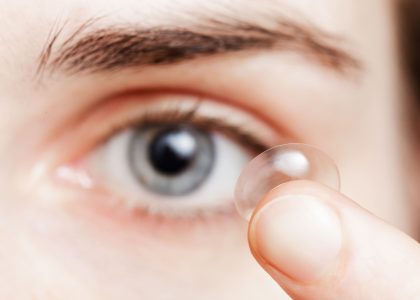 A woman is holding contact lenses in her eye.