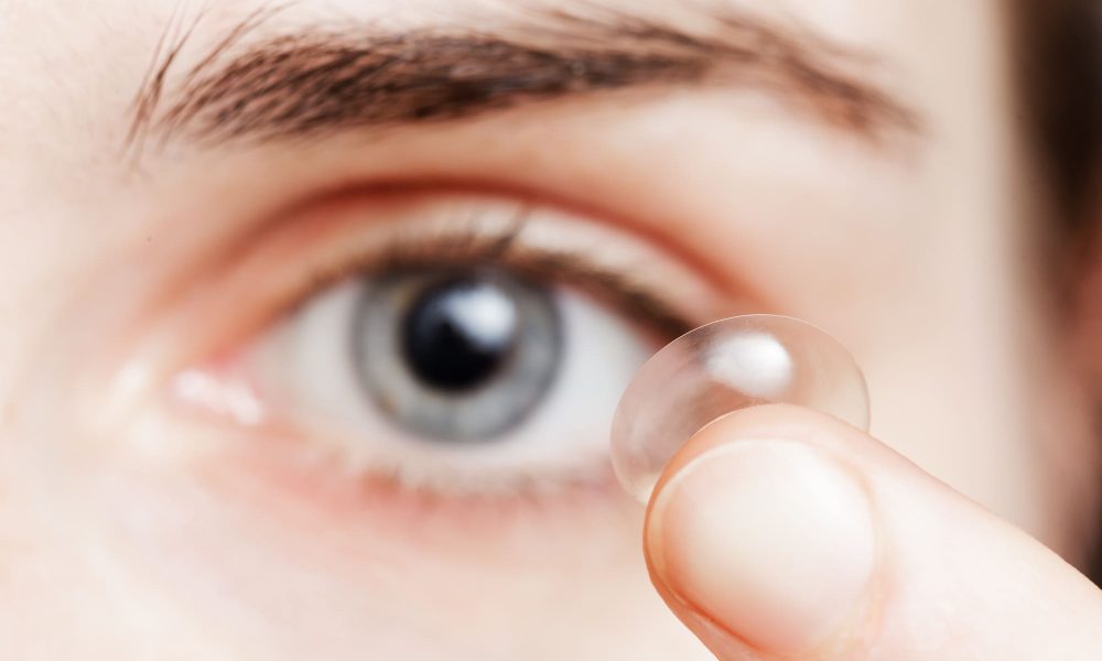 A woman is holding contact lenses in her eye.