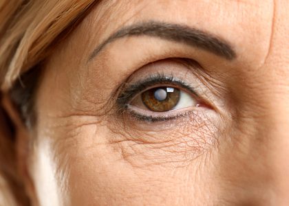 Close-up of a mature person's eye, highlighting detailed wrinkles around the area and slightly arched eyebrow. The eye, open and looking straight ahead, shows no symptoms of cataracts.