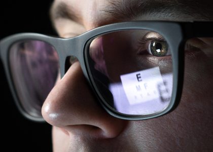 Close-up of a person wearing glasses, with an eye chart visible in the reflection of the lenses.