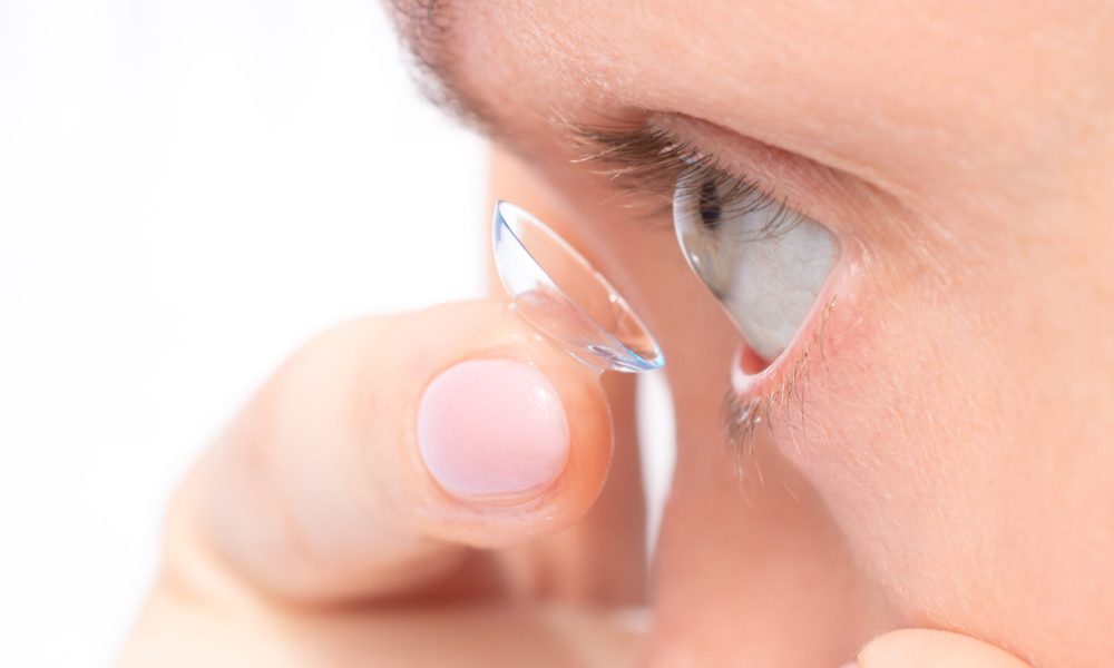 Close-up of a person inserting a contact lens into their eye using fingertips, showing careful placement.