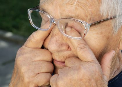 An elderly person wearing glasses rubs their eyes with their fingers outdoors, possibly seeking relief from itchy eyes. For those experiencing similar discomfort, The Eye Pros offer expert advice on relieving itchy eyes effectively.