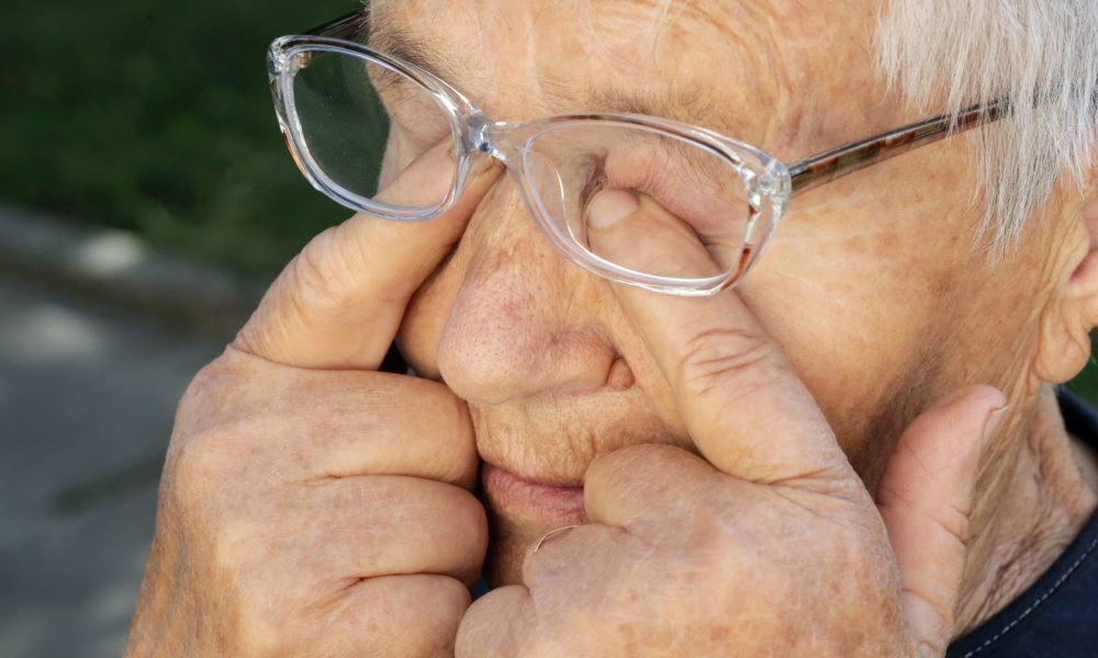 An elderly person wearing glasses rubs their eyes with their fingers outdoors, possibly seeking relief from itchy eyes. For those experiencing similar discomfort, The Eye Pros offer expert advice on relieving itchy eyes effectively.