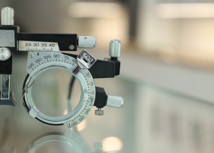 Close-up of a metal optical trial frame with adjustable dials, set on a reflective surface.