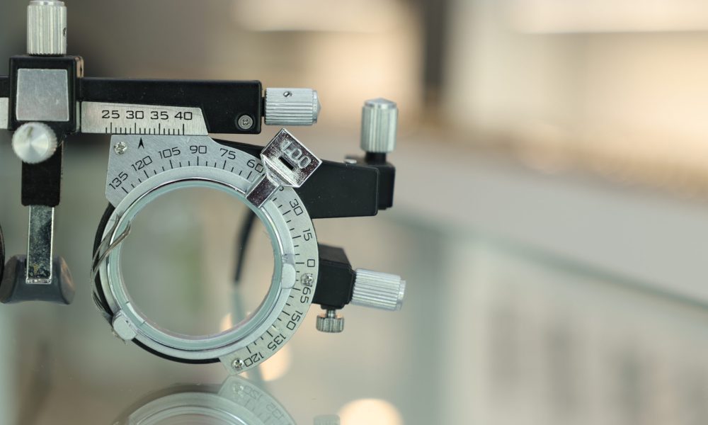 Close-up of a metal optical trial frame with adjustable dials, set on a reflective surface.