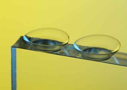 Two contact lenses, like tiny mirrors, rest on a reflective surface against a vibrant yellow background. It's crucial to consider the realities of wearing expired contacts to avoid potential risks to your eye health.