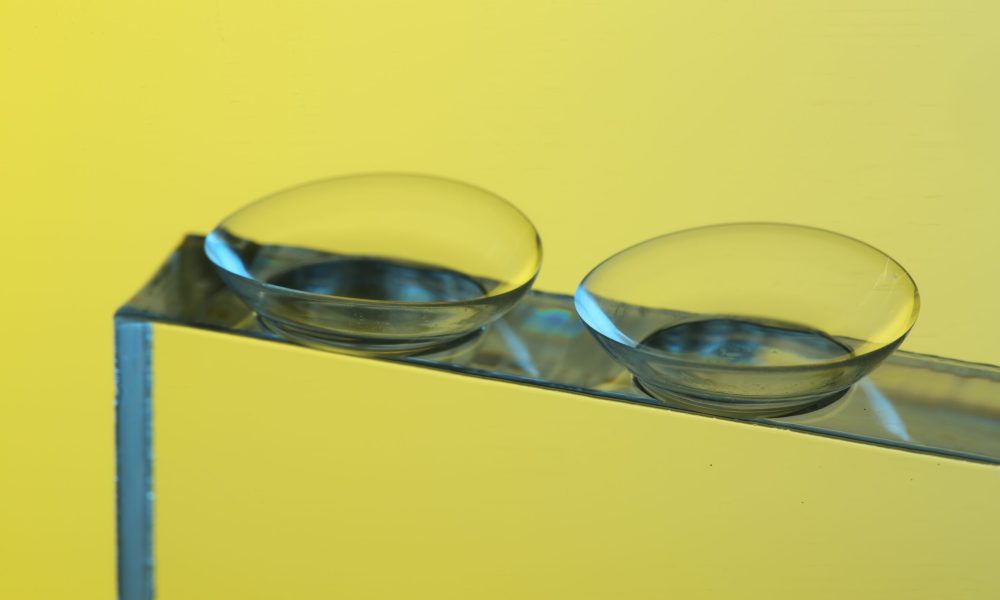 Two contact lenses, like tiny mirrors, rest on a reflective surface against a vibrant yellow background. It's crucial to consider the realities of wearing expired contacts to avoid potential risks to your eye health.