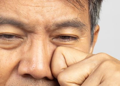 Close-up of a person rubbing their eye with a fist, appearing tired—a common cause of discomfort like dry eyes.