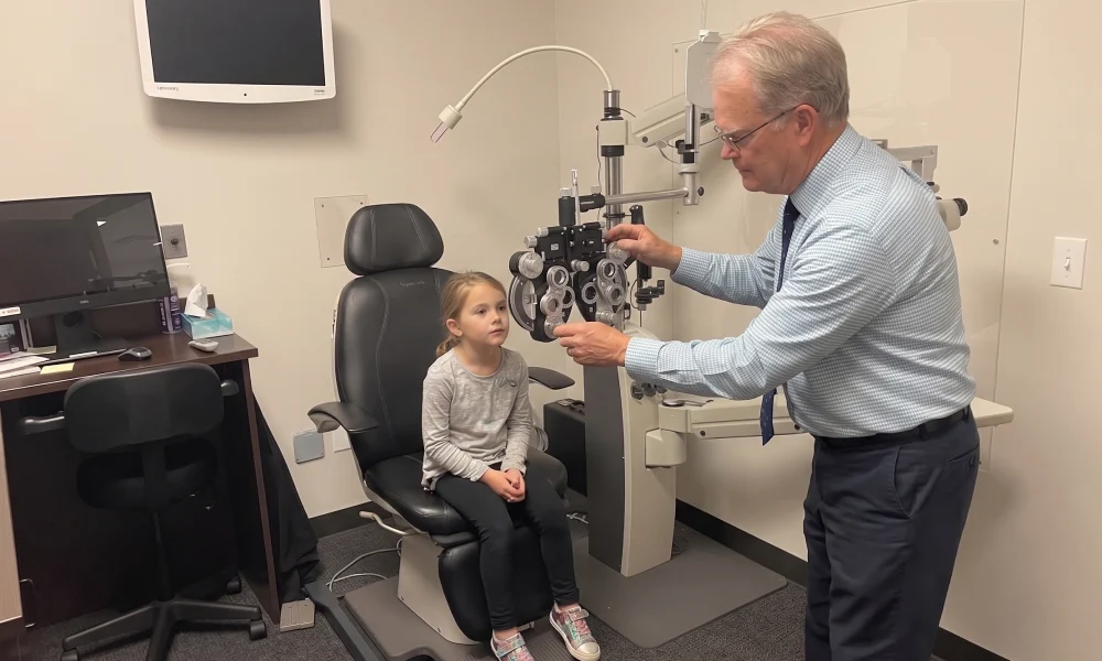 Optometrist performing an eye exam on a young patient using a phoropter in the Layton office.
