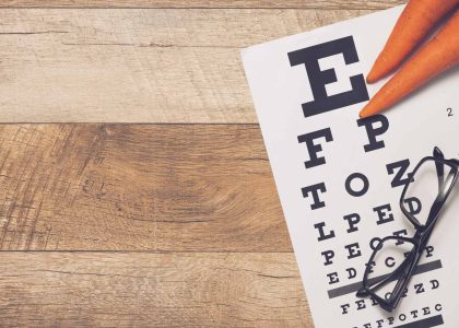 Eye care chart with carrots and glasses on a wooden table.