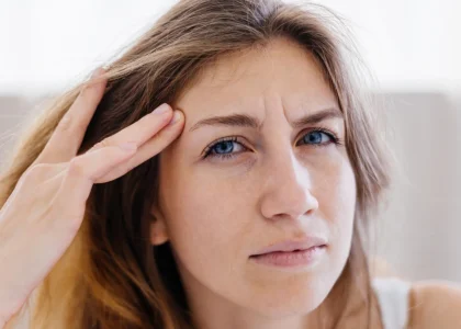 Woman touching her temple with a concerned expression, illustrating discomfort associated with eye strain or dry eyes.