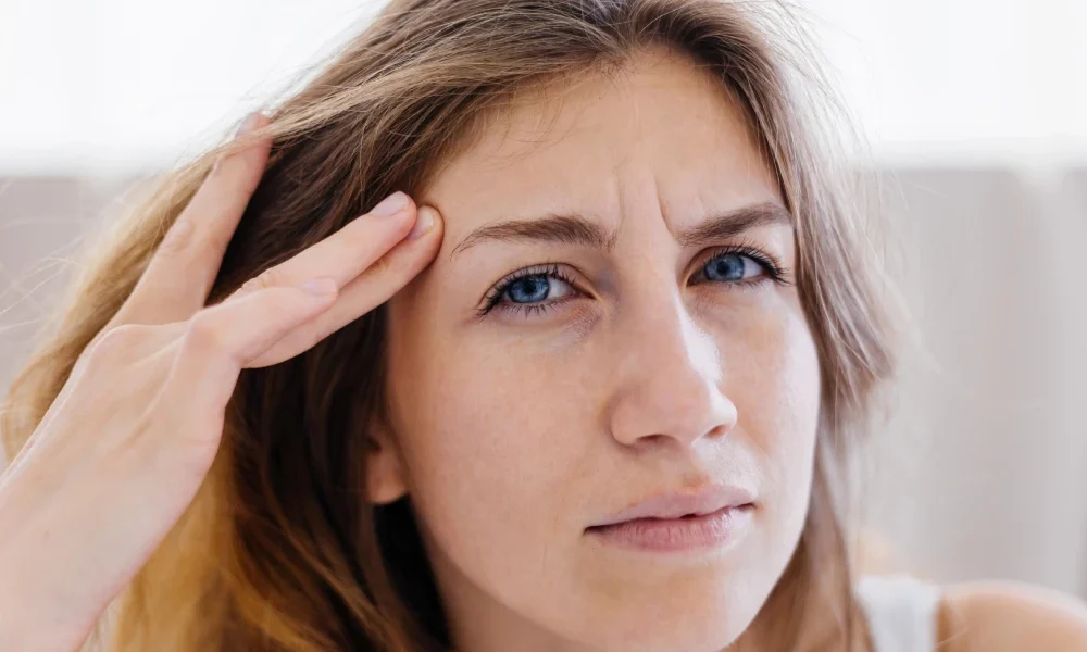 Woman touching her temple with a concerned expression, illustrating discomfort associated with eye strain or dry eyes.