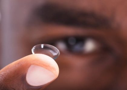 A man is holding up a small contact lens, wondering can a contact get lost in your eye.