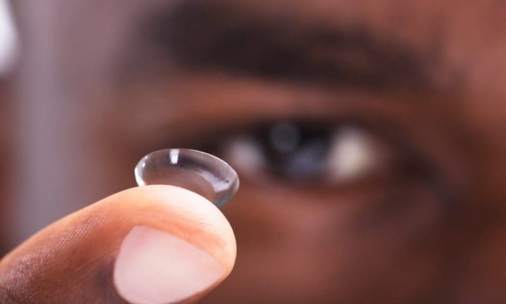 A man is holding up a small contact lens, wondering can a contact get lost in your eye.