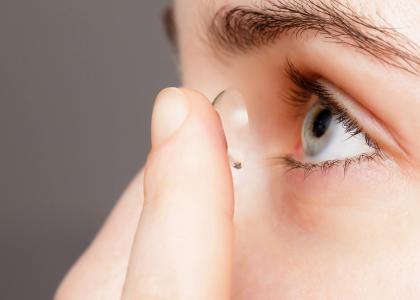 A person in Coeur d’Alene holds a contact lens close to their blue eye, preparing to insert it for enhanced comfort and looks.
