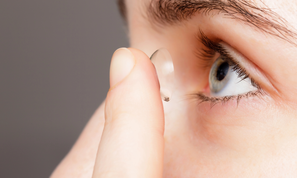 A person in Coeur d’Alene holds a contact lens close to their blue eye, preparing to insert it for enhanced comfort and looks.